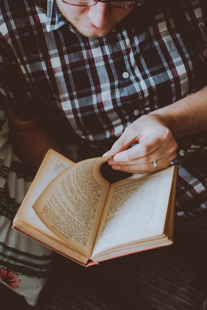 who-we-are Adult male wearing plaid shirt reading a book indoors for leisure and relaxation.