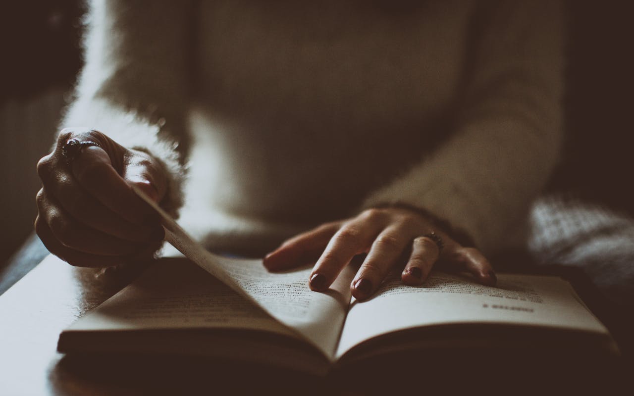 A person is reading a book in moody lighting, creating an intimate and reflective atmosphere.