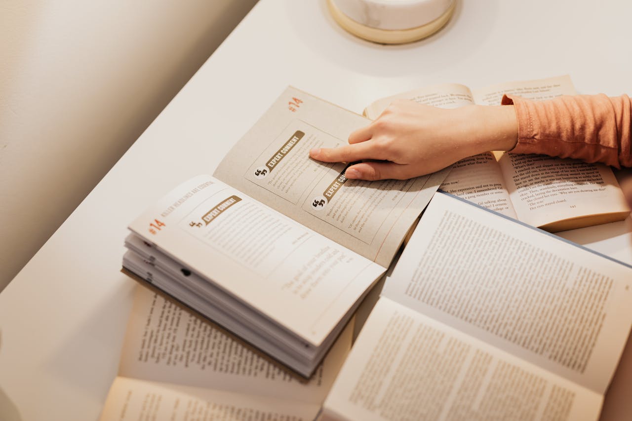 Woman's hand pointing to text in open books, symbolizing study and learning.
